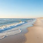 Pristine white sand beach with gentle waves and blue sky, empty shoreline stretching into distance during peaceful winter day