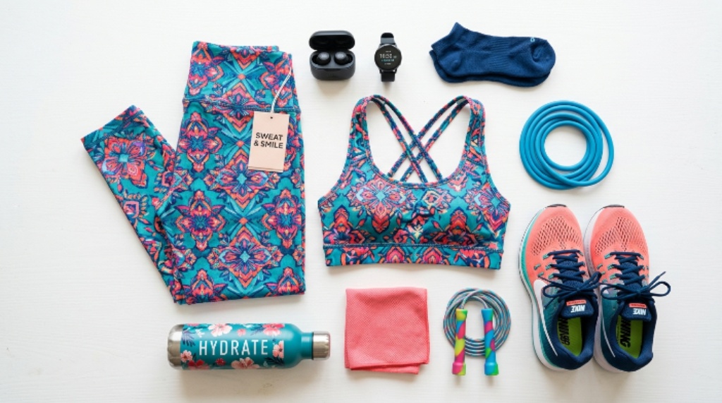 A flat lay of colorful women’s activewear including leggings, a sports bra, and running shoes on a white background