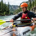 Kayaker securing paddle with a coiled leash on a calm river.